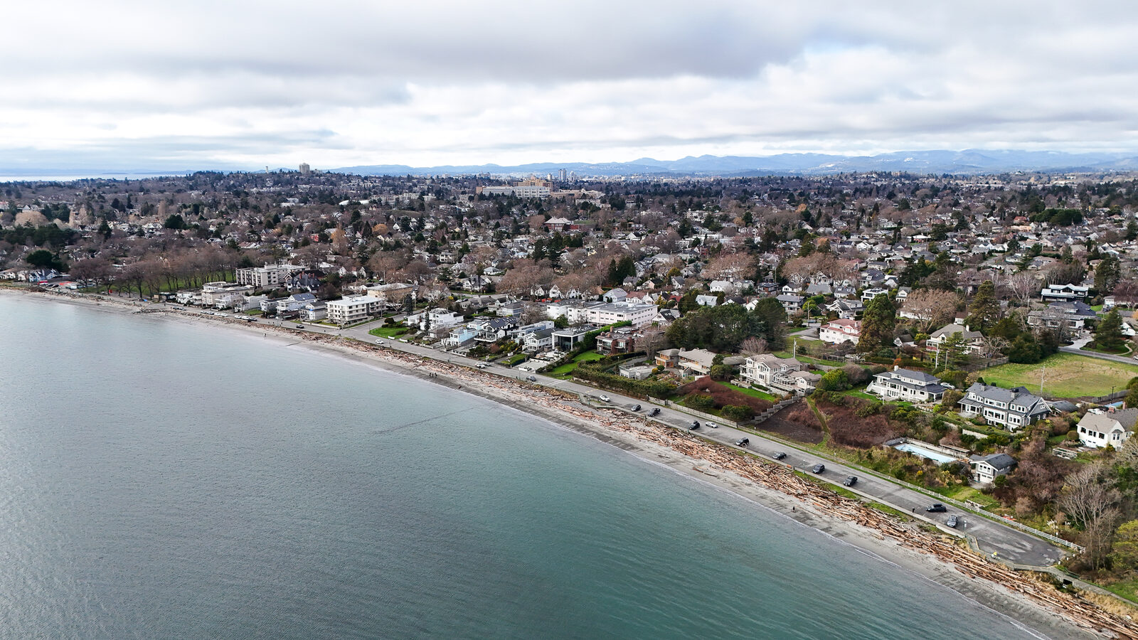 Aerial view of the Oak Bay shoreline with driftwood along the beach and homes facing the water.